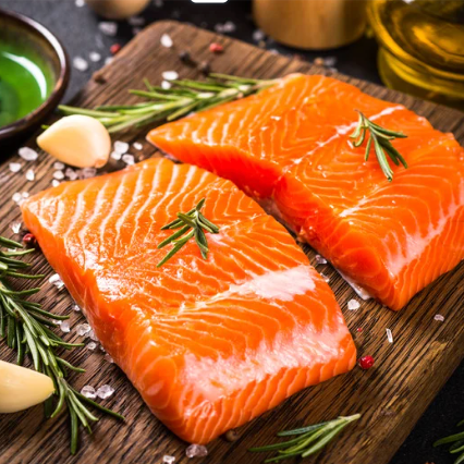 Two raw salmon fillets on a wooden cutting board with rosemary and garlic.