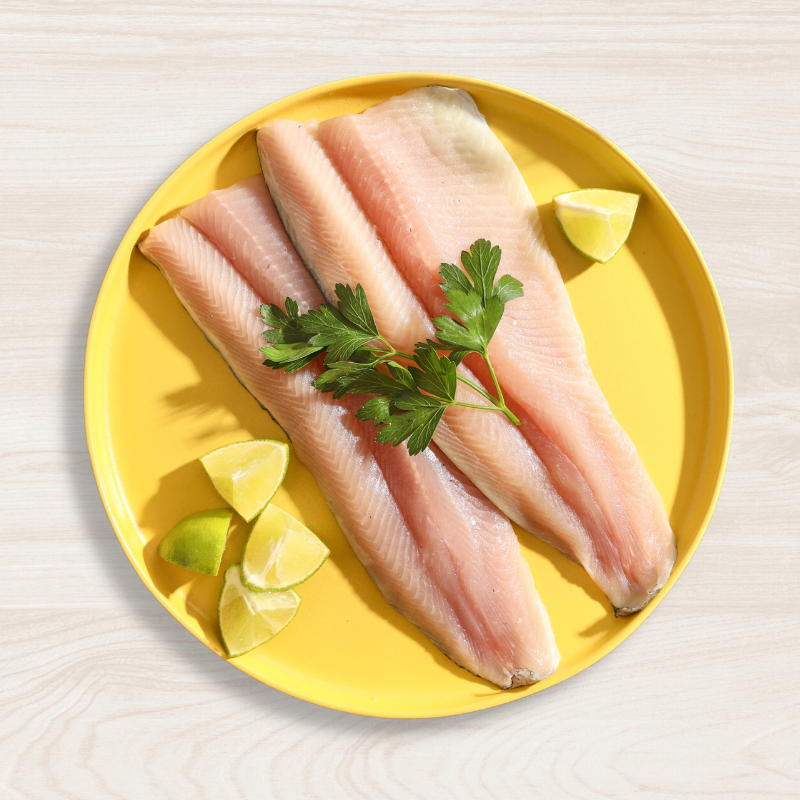 Two fresh Rainbow Trout fillets on a yellow plate with lemon wedges and parsley leaves.